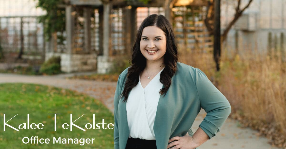 A woman with long dark hair, Kalee TeKolste, wearing a light blue blazer and white top, stands smiling outdoors near a path with autumn foliage. Text on the image reads: "Kalee TeKolste, Office Manager.