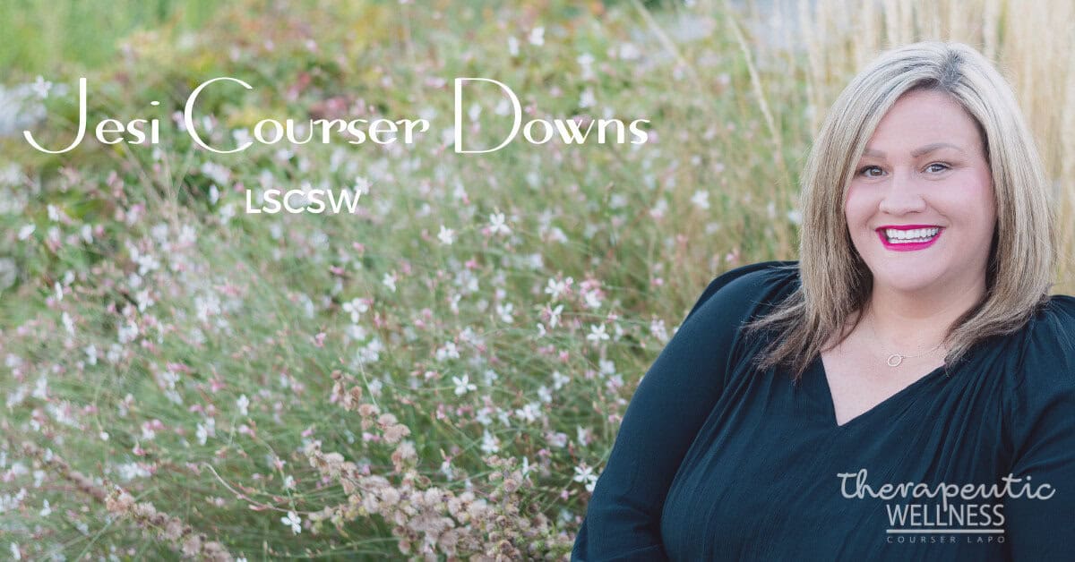 A smiling woman with long hair sits in front of a garden adorned with small white flowers. Text on the image reads "Jesi Courser LSCSW" and "Therapeutic Wellness Lab." Jesi Downs dons a black top and red lipstick, exuding an aura of calm confidence.