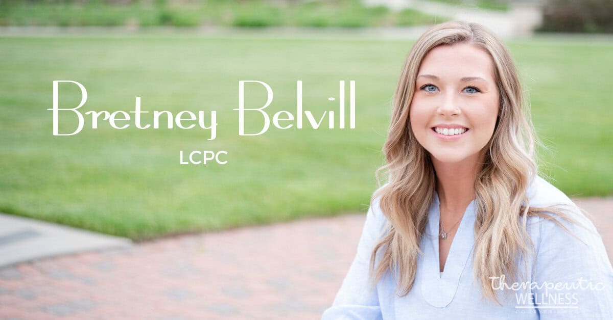 A woman with long blonde hair and a blue shirt smiles in an outdoor setting. The text on the image reads "Kali Harvey, LCPC" in large font and "therapeutic wellness" in smaller font at the bottom right corner. The background features grass and a walkway.