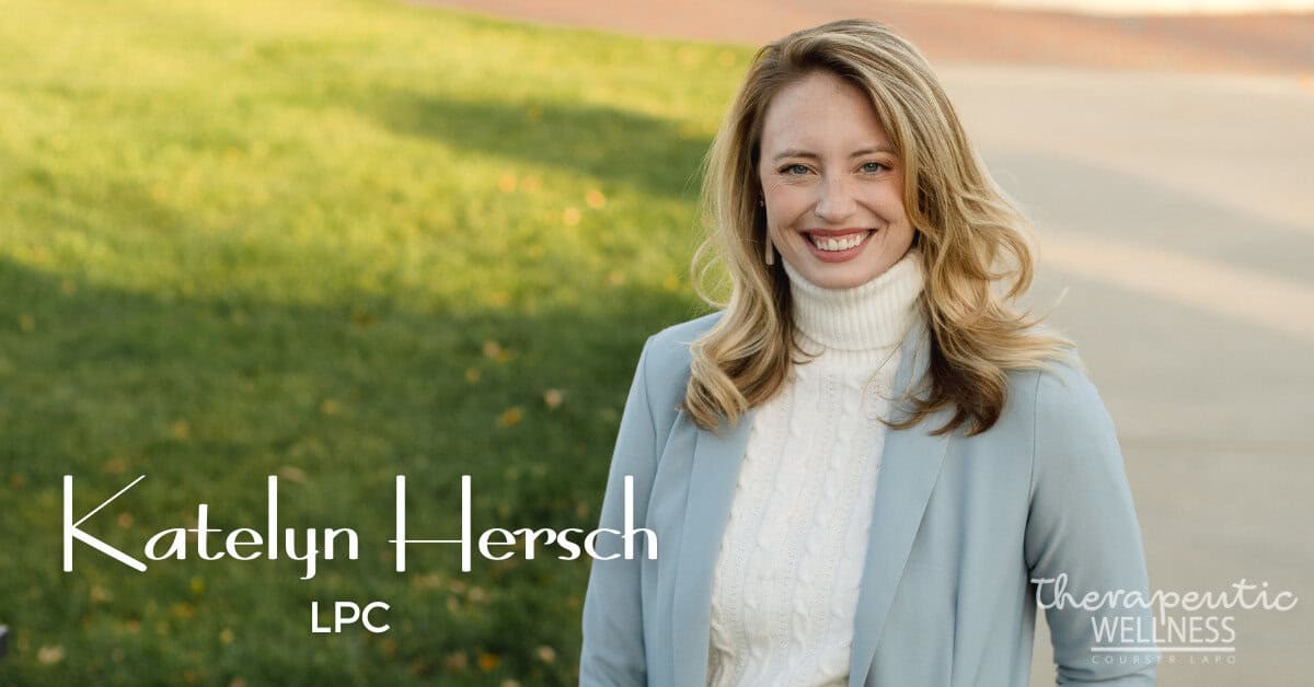 A woman with long blonde hair, wearing a light blue blazer and a white turtleneck, smiles outdoors. The text reads "Katelyn Hersch," showcasing "Therapeutic Wellness Counseling." The background features a green lawn and a walkway.