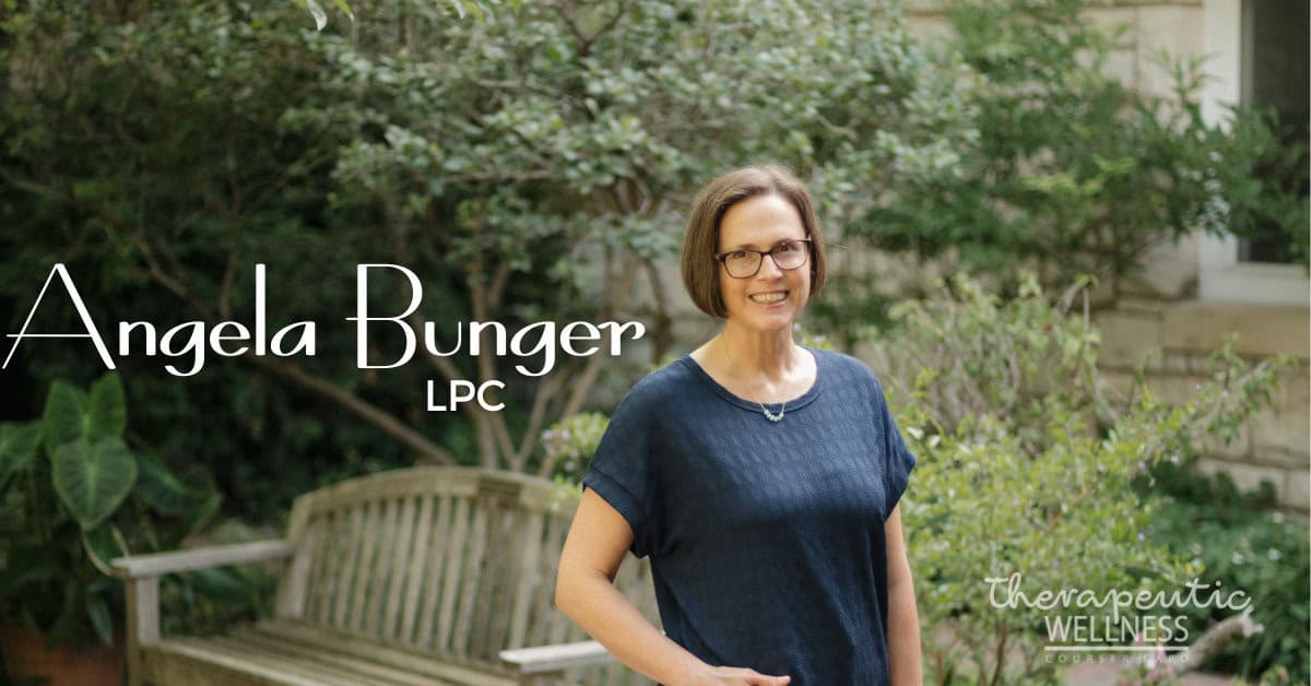 A woman with short brown hair and glasses stands smiling outdoors near a wooden bench, surrounded by greenery. Text on the image reads &ldquo;Angela Bunger, LPC,&rdquo; highlighting her dedication to therapeutic wellness counseling.