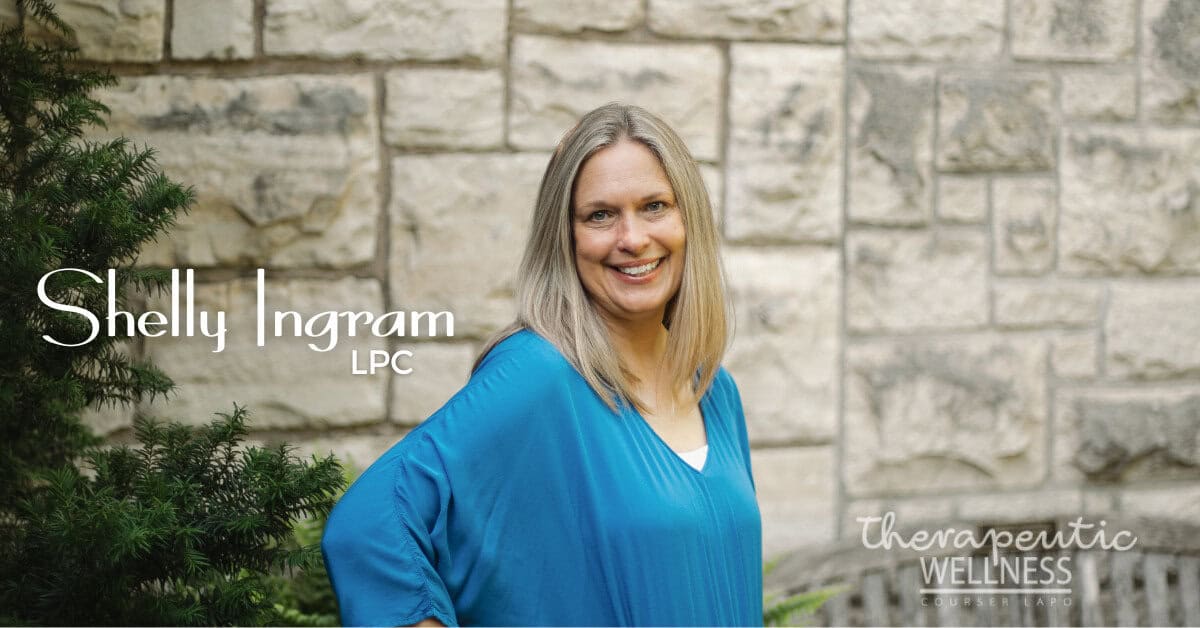 Shelly Ingram, with straight blonde hair and a blue top, stands smiling in front of a stone wall. Text reads &ldquo;Shelly Ingram, LPC&rdquo; and &ldquo;Therapeutic Wellness,&rdquo; with green leafy plants on the left.