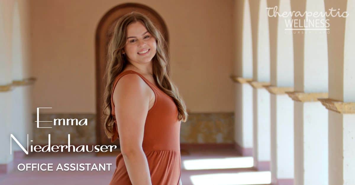Emma Niederhauser, a young woman with long brown hair in a sleeveless orange dress, smiles warmly while standing in a sunlit hallway. Text reads: "Emma Niederhauser, Office Assistant, Therapeutic Wellness.