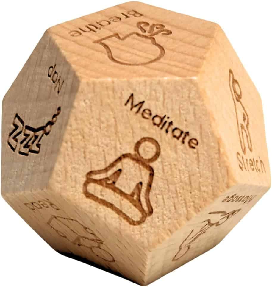 A wooden twelve-sided die with different wellness activities engraved on each face, including meditate, stretch, hydrate, rest, and a few simple illustrative icons.