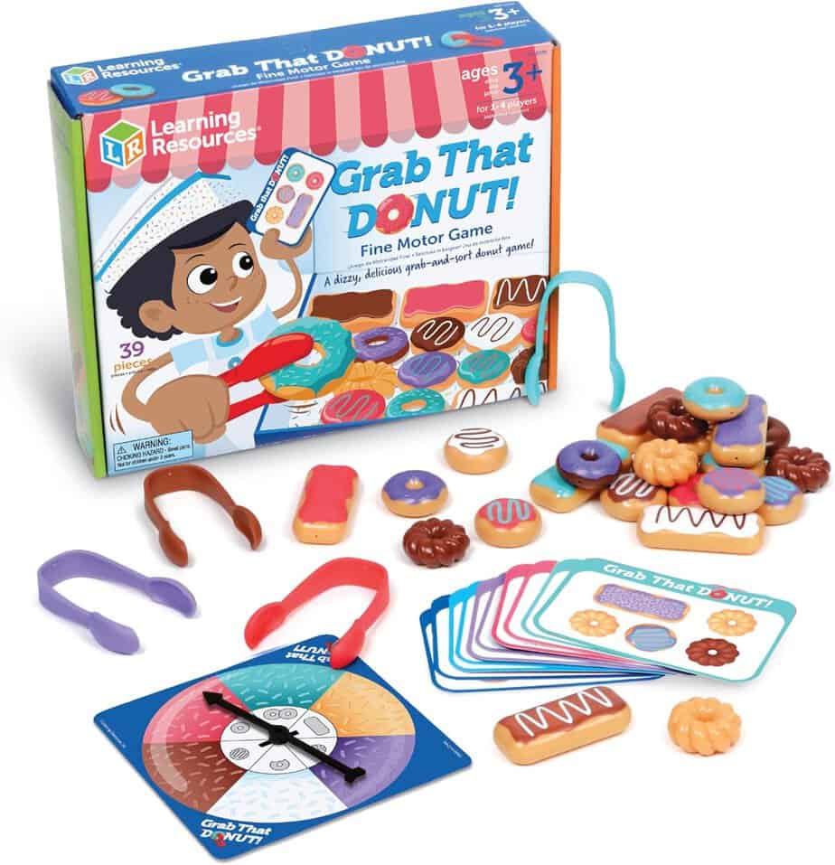 A colorful children&rsquo;s game called "Grab That Donut!" featuring a game box, plastic donuts, tongs, playing cards like Go Together Flashcards, and a spinner for fine motor skill development. Perfect for ages 3 and up.