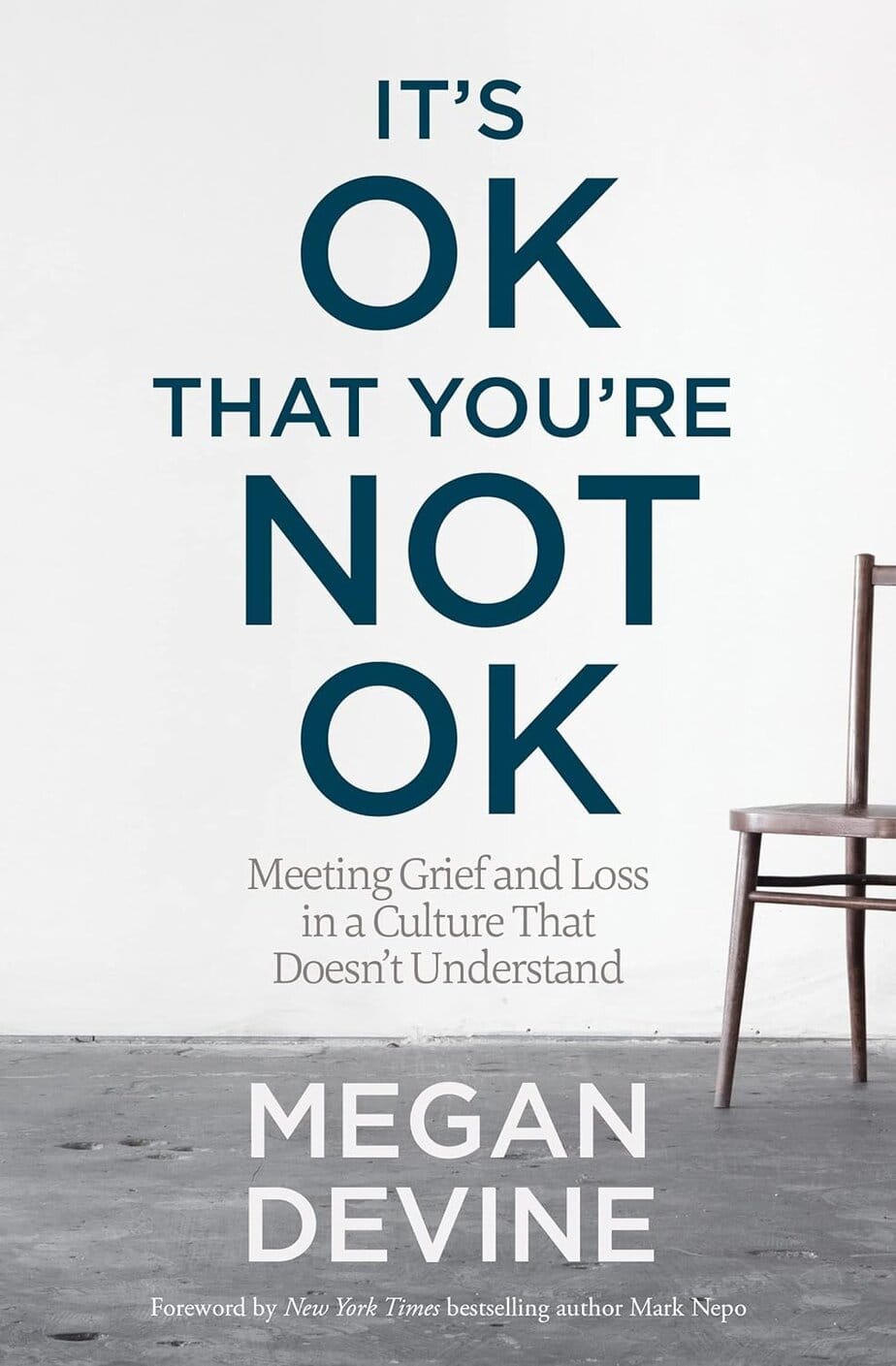 The book cover for "It's OK That You're Not OK" by Megan Devine features the title in large blue text above a partially visible empty wooden chair on a gray concrete floor, reflecting the book's message of acceptance. Subtitles and author&rsquo;s name appear below.