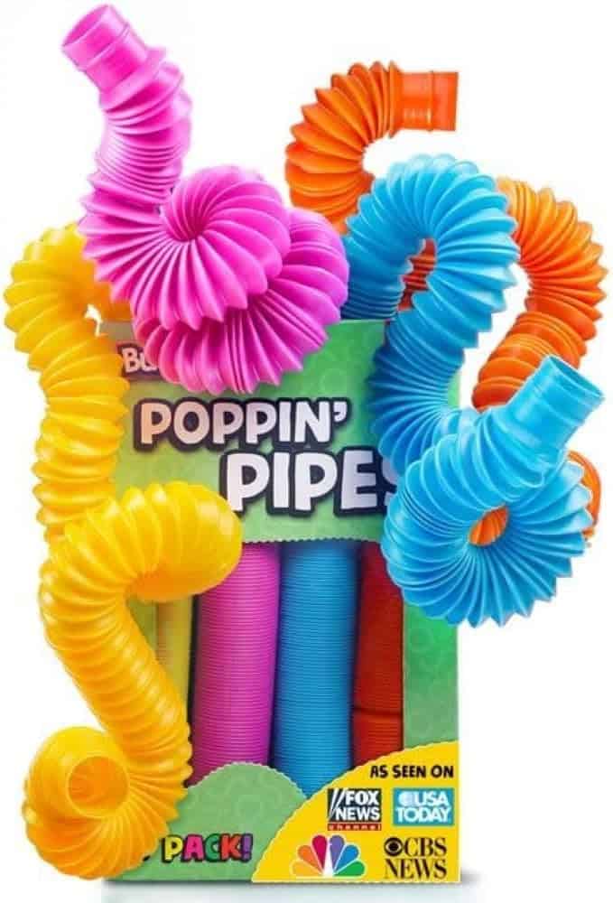 Colorful expandable pop tubes in yellow, orange, blue, and pink are arranged in and around a box labeled "Poppin' Pipe Pack!" with logos from NBC, Fox News, USA Today, and CBS News on the packaging.