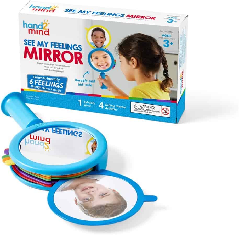 A set called "See My Feelings Mirror" by hand2mind is shown. It includes a blue-handled mirror and a box displaying images of children expressing different emotions, designed to help kids identify feelings.